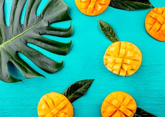 Wall murals Turquoise Creative layout made of summer tropical fruits mango and tropical leaves on turquoise background. Flat lay. Food concept. Tropical concept