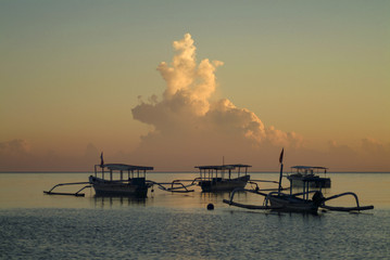 Naklejka premium Balinese Outrigger Boats Anchored Off the Village of Pemuteran During a Glorious Sunrise. A thunderhead on the horizon provides the background to a tropical paradise in the Indian Ocean.