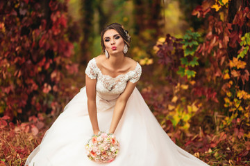 Fototapeta na wymiar Beautiful bride standing at colorful autumn forest and sending a Kiss