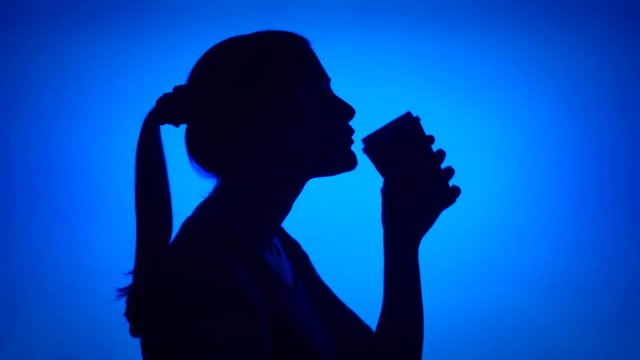 Silhouette of young woman using mobile on blue background. Female's face in profile chatting with friend on cellphone. Black contur shadow of teenager's half-face talking