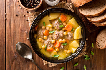 Soup with meatballs, vegetables and chickpea on wooden table