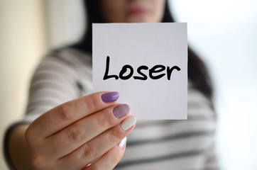 Young sad girl shows a white sticker. Caucasian brunette holding a sheet of paper with message....