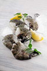 fresh king prawns with lemon and lemon balm on white wooden kitchen plate can be used as background