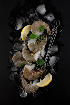 fresh raw king prawns with lemon and lemon balm on dark slate kitchen plate with napkin can be used as background