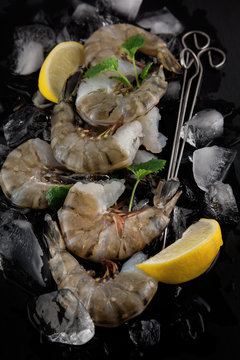 fresh raw king prawns with lemon and lemon balm on dark slate kitchen plate with napkin can be used as background