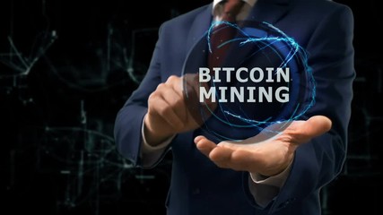 Businessman shows concept hologram Bitcoin Mining on his hand. Man in business suit with future technology screen and modern cosmic background