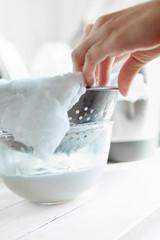 woman preparing vegan almond or coconut milk at home. Pouring the milk into a cheese cloth to filter it.