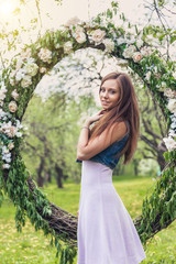 Fototapeta na wymiar девушка с длинными волосами в весеннем саду с цветущими яблонями на фоне венка с цветами