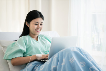 Asian woman sick patient lying in a hospital bed using a laptop for relax when she recovering for...