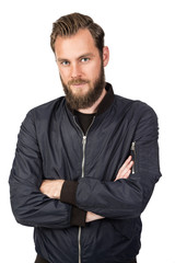 Handsome bearded man standing against a white background wearing a black tshirt and blue jacket in jeans with arms crossed. Looking at camera.