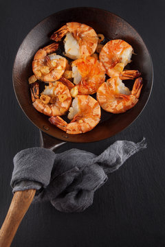 fresh prepared king prawns in an iron pan with garlic on dark slate kitchen plate can be used as background