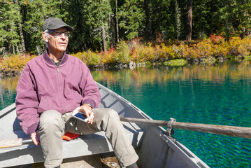 Handsome senior man in row boat with cell phone on a beautiful autumn day