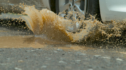 CLOSE UP: Murky water splashes across asphalt road as car drives into puddle.