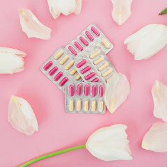 Medical composition with vitamins pill and white flowers on pink background. Flat lay, top view.