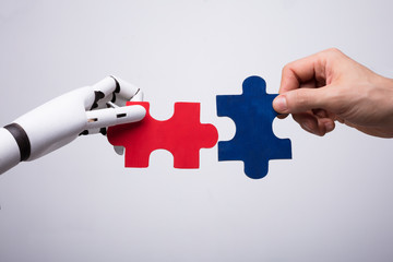 Robot And Human Hand Holding Jigsaw Puzzle