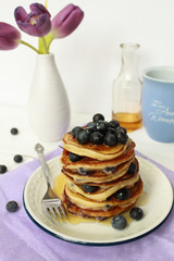 Stack of Healthy Pancakes with Maple Syrup and Blueberries. Lilac background, violet tulips in a vase on the table, breakfast concept, copy space