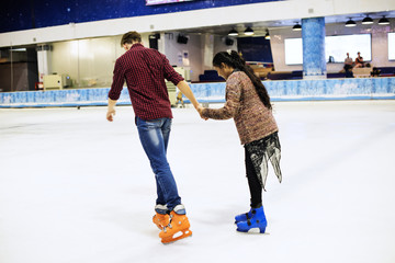 Teenage couple holding hands and ice skating together