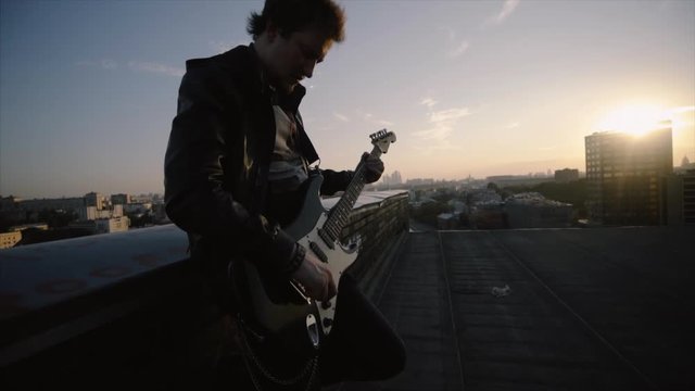 men in rock n roll style standing on the roof and playing on guitar at cityscape background