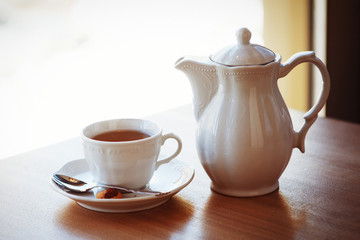 A white kettle and a cup with a saucer and a teaspoon are on the table