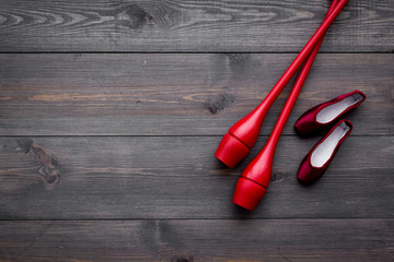 Beauty sport for girls concept. Maces for rhythmic gymnastics and ballet shoes on dark wooden background top view copy space