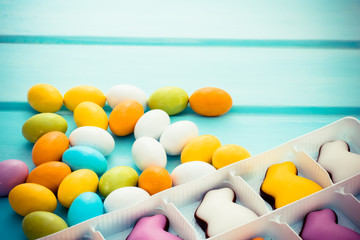 Scattered easter colorful sweet chocolate small eggs with candy bunnies on blue background. Copyspace