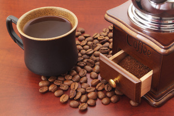 Coffee grinder with roasted coffee beans and cup of coffee on table close up