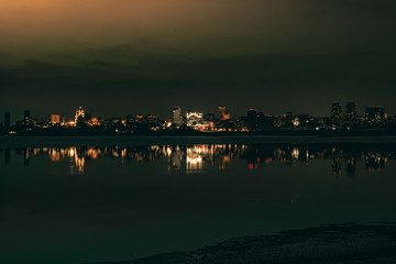 Night city view with lots of lights and its reflection in a river water
