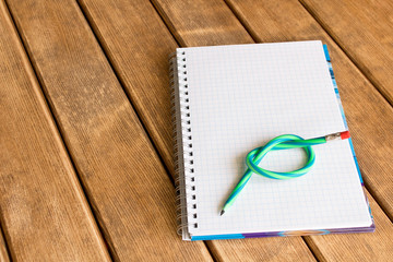 A bent pencil on a notebook . On wooden background