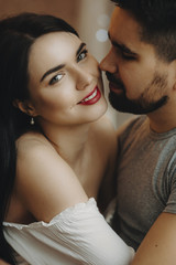 Portrait of an adult woman with red lips hugging her man and looking at the camera.