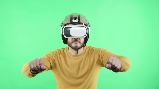 One young guy in wearable emulator spectacles playing cyberspace game standing in chromakey greenbox close up isolated. Male person in vr-glasses enjoyment alone, motorcyclist rider at motorbike