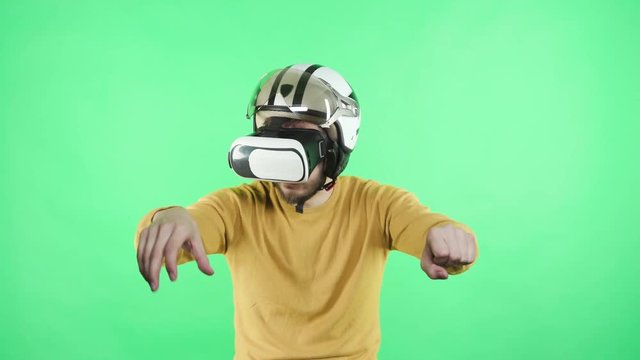 One young guy in wearable emulator spectacles playing cyberspace game standing in chromakey greenbox close up isolated. Male person in vr-glasses enjoyment alone, motorcyclist rider at motorbike