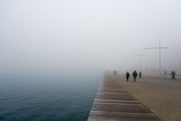 People walking on the waterfront of Thessaloniki, Greece, on a foggy day