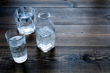 Drinking water in bottles and glasses on dark wooden background copy space
