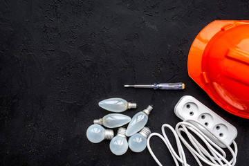 Electrical installation, wiring work concept. Hard hat, bulb, socket outlet on black background top...