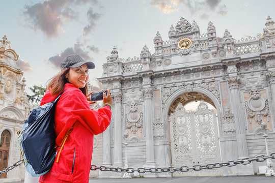 Tourist woman taking photo on her smartphone at the main entrance gate of Dolmabahce Palace