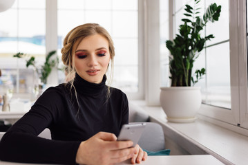 Pretty student sitting in cafe and looking at phone.