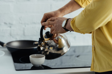 Man pouring hot water in cup on kitchen table