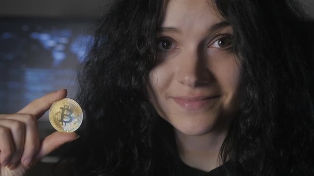 Young woman with curly hair holds gold Bitcoin in hand. Mining and trading