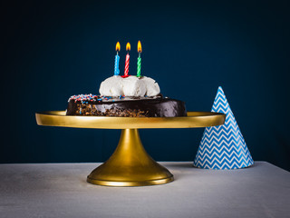Three candles in chocolate cake  on golden tray and dark blue ba - obrazy, fototapety, plakaty