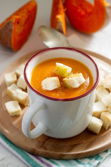 Delicate vegetable cream soup with pumpkin and croutons and slices of pumpkin on a light background.