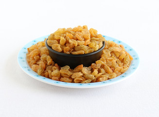 Raisins or dry grapes, organic type, healthy vegetarian food, in a bowl on a plate with spilled raisins.