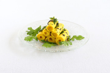Khandvi, a roll made from chickpea flour and yogurt, is an Indian vegetarian snack tempered with items like mustard, green chilies and curry leaves, stacked on a glass plate. © Greentree
