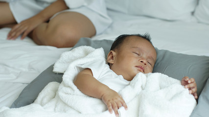 Young beautiful Asian mother caring and playing with her baby in the bedroom on a bright morning sunshine