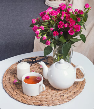 Herbal tea, pink roses, candle on the white coffee table.