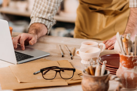 cropped view of male potter using laptop in workshop