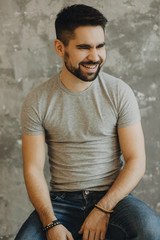 Portrait shot of handsome young man with a beard looking and smiling into the camera on a gray background.