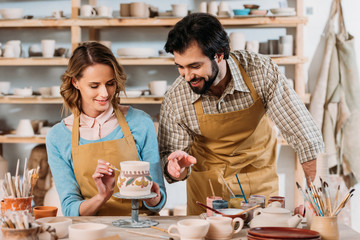 potters painting traditional ceramic jug in workshop