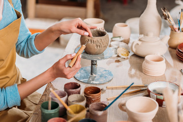 cropped view of female potter decorating ceramic bowl in workshop