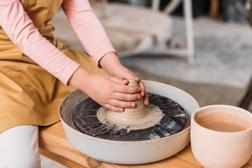 cropped view of child with clay learning to use pottery wheel