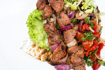 Traditional Greek souvlaki barbecue skewer with cabbage and tomato onion salad as top view on phyllo bread with copy space left - covered